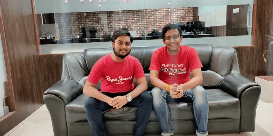 Two teammates in red t-shirts sitting on an office sofa