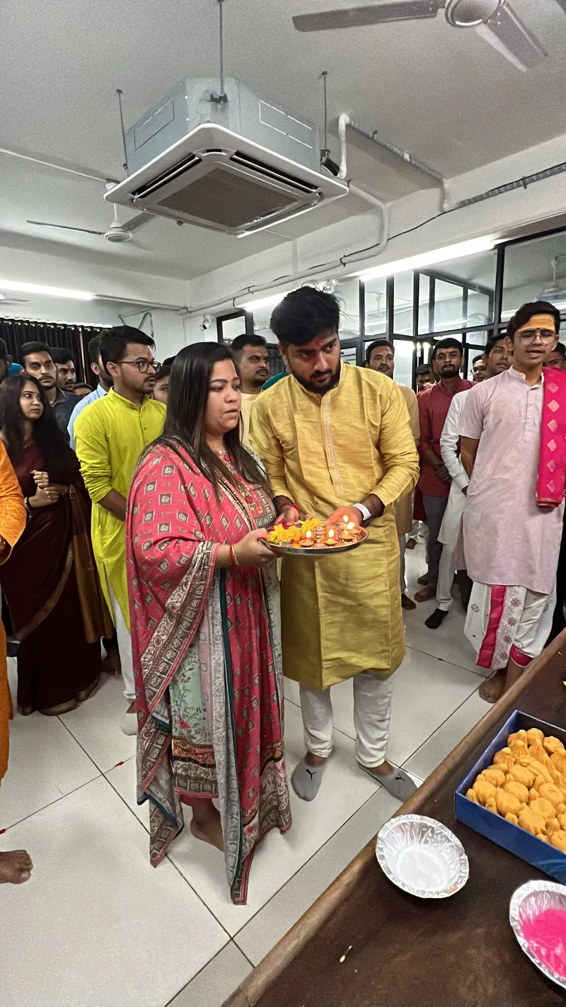 Teammates holding an aarti plate during the Ganesh puja with colleagues gathered behind them in the office
