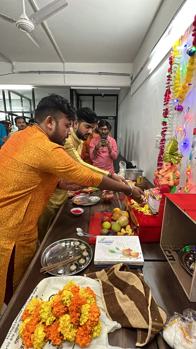 Teammates in kurtas performing the Ganesh puja in the office while colleagues watch
