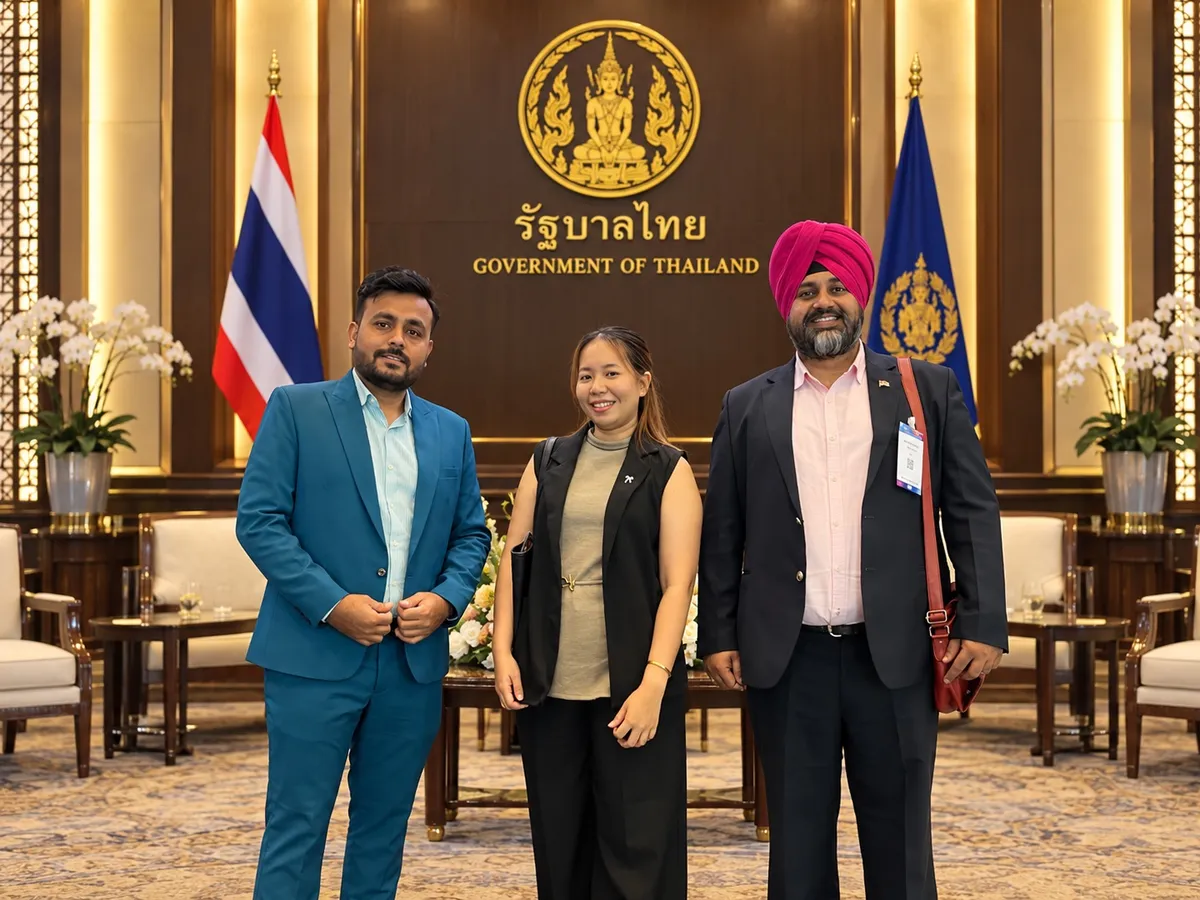 Three people posing in front of a Government of Thailand sign with flags and orchids